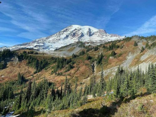 A majestic snow-capped mountain rises above a lush green landscape under a clear blue sky.