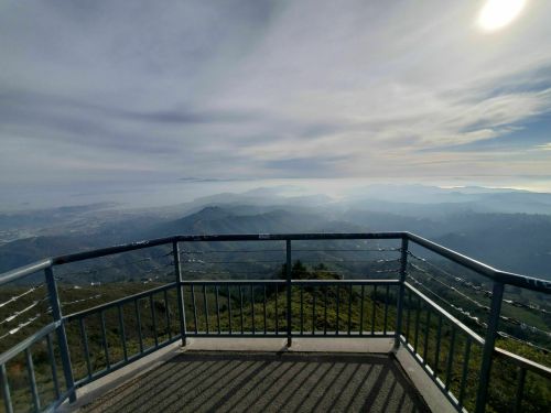 View from a mountain overlook, featuring rolling hills and a hazy landscape under a cloudy sky.
