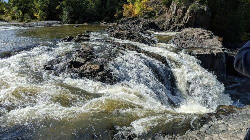 A rushing waterfall cascades over rocky terrain, surrounded by lush greenery and autumn-colored trees.