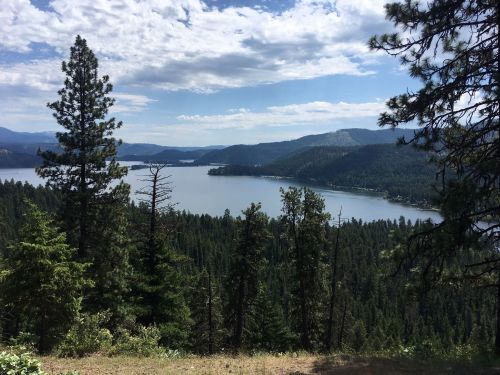 A scenic view of a lake surrounded by lush green forests and mountains under a partly cloudy sky.