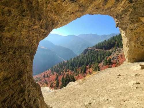 View through a rocky archway overlooking a colorful valley with mountains in the background under a clear blue sky.