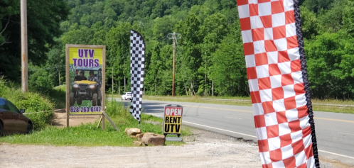 Signage for UTV tours with checkered flags along a roadside in a green, wooded area.