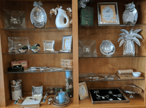 A wooden display shelf filled with decorative items, including glassware, silver accents, and framed pictures.