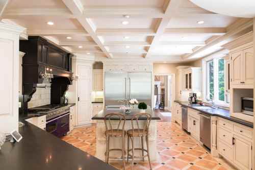 Modern kitchen with a coffered ceiling, large island, stainless steel appliances, and warm tile flooring.