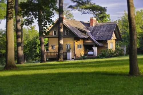 A charming yellow house surrounded by trees and a lush green lawn, set in a serene outdoor environment.