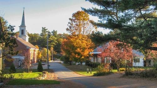 A peaceful street scene with autumn trees, a church steeple, and charming houses under a clear sky.