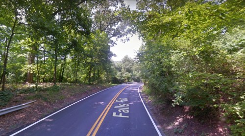A winding road named Falls Rd surrounded by lush green trees and foliage.