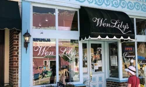 A storefront with a black awning reading "Wen Lily's," featuring large windows and a person sitting outside.