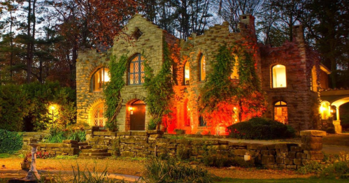 A stone house surrounded by trees, illuminated with warm lights and adorned with climbing vines, creating a cozy atmosphere.