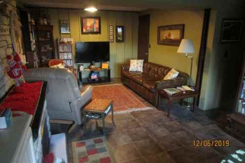 Cozy living room with a brown leather sofa, armchair, TV, and decorative items on the walls and shelves.