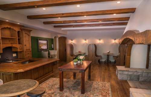 Cozy interior with wooden beams, a kitchen area, a table, and seating nooks, featuring warm lighting and rustic decor.