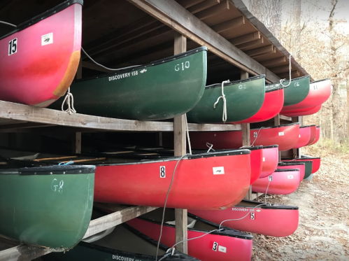 Canoes stacked on a wooden rack, featuring green and red colors, with numbers visible on each canoe.