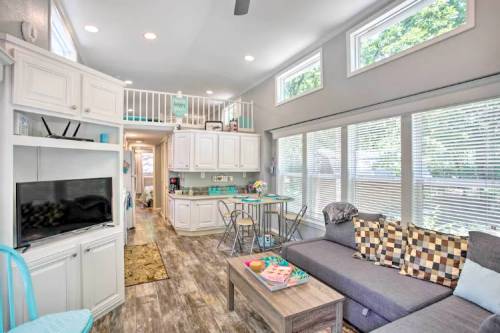 Bright, modern living space with a sofa, coffee table, and kitchen area, featuring large windows and light wood flooring.