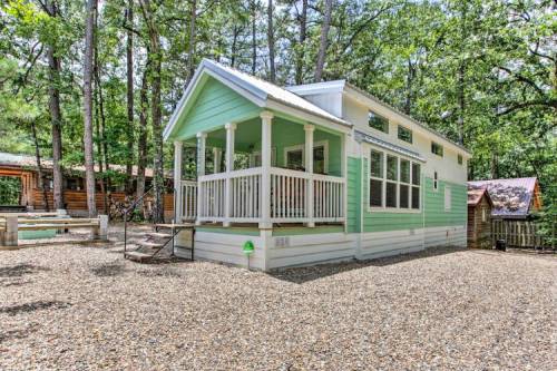 A small, light green house with a porch, surrounded by trees and gravel, in a serene outdoor setting.