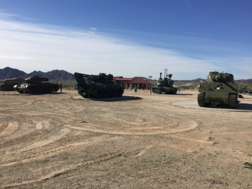 Four military tanks displayed outdoors with mountains in the background under a clear blue sky.