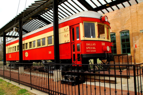 A vintage red and cream train car, labeled "Dallas Special," displayed under a canopy at a historical site.