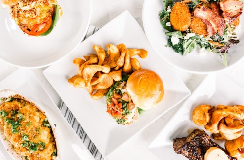 A variety of dishes including a burger, salad, pasta, and curly fries arranged on white plates.