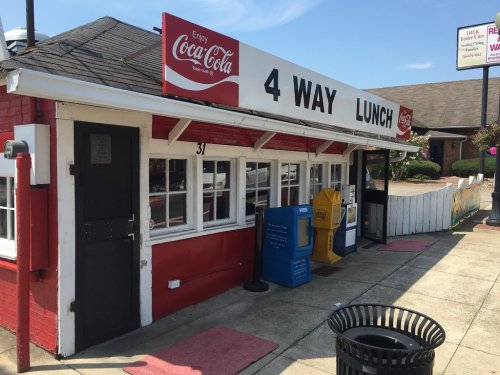Exterior of a red and white diner named "4 Way Lunch," featuring large windows and a Coca-Cola sign.
