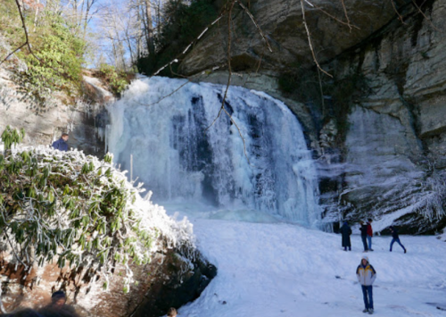A frozen waterfall surrounded by snow, with people exploring the area in a winter landscape.