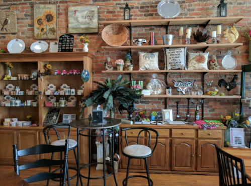 A cozy shop interior with brick walls, wooden shelves displaying decor, plants, and various products for sale.