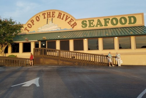 Exterior of Top O' the River Seafood restaurant with a ramp and two people walking towards the entrance.