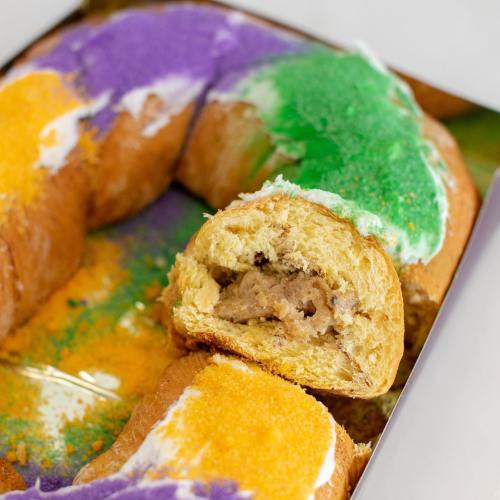 A colorful king cake with purple, green, and orange icing, showcasing a slice revealing a creamy filling inside.