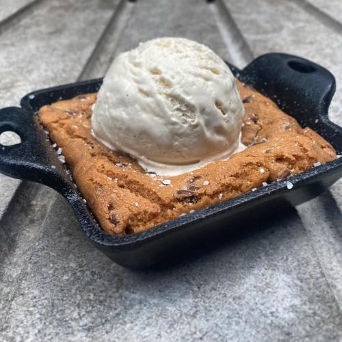 A warm cookie skillet topped with a scoop of vanilla ice cream, served in a small cast iron pan.