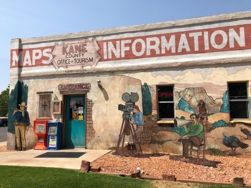 A colorful building with murals depicting tourists and a film crew, featuring a sign for the Kane County Office of Tourism.