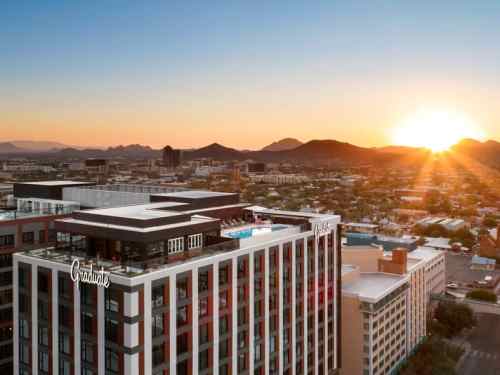 Aerial view of a modern hotel at sunset, with mountains and city skyline in the background.