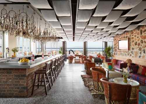 A stylish bar with a cozy seating area, featuring dreamcatchers and a scenic view through large windows.