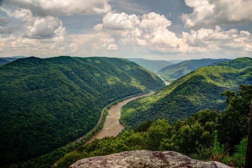 A scenic view of lush green mountains surrounding a winding river under a partly cloudy sky.