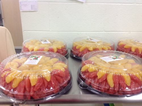 Four fruit trays with a mix of red and yellow melon slices, each covered with a clear plastic lid.