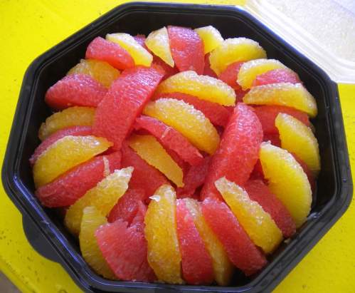 A black container filled with vibrant slices of red and yellow grapefruit arranged in a circular pattern.