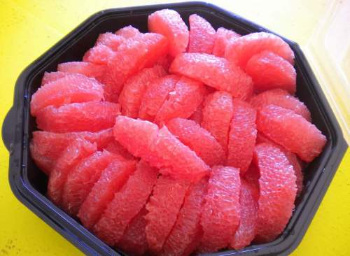 A black container filled with neatly arranged pink grapefruit segments.