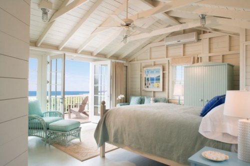 Bright coastal bedroom with a large bed, light blue decor, and open doors leading to a scenic ocean view.