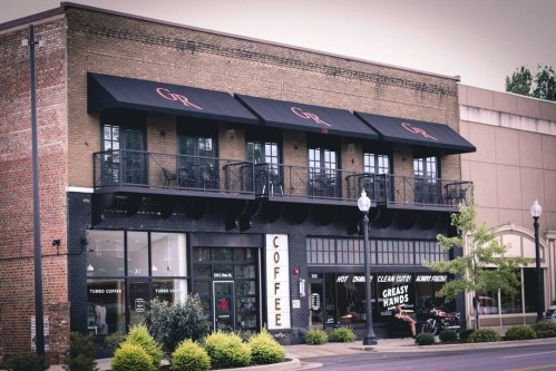A coffee shop with large awnings and outdoor seating, featuring a sign that reads "COFFEE" and "GREASY HANDS."