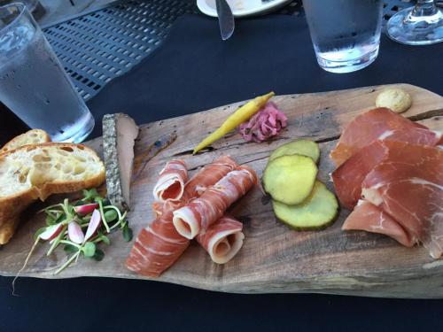 A wooden platter with assorted cured meats, pickles, bread, mustard, and garnishes, set on a black tablecloth.