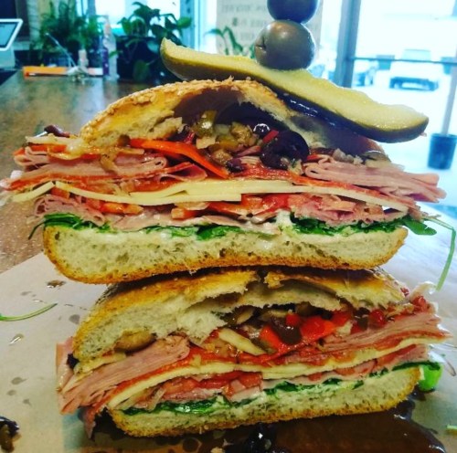 A towering sandwich stacked with layers of meats, cheese, and vegetables, topped with an olive and pickle.