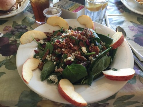 A fresh salad with spinach, apples, pecans, bacon, and blue cheese, served on a white plate.
