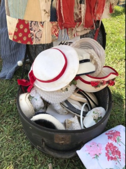 A vintage suitcase filled with various hats, including straw and decorative styles, resting on grass.