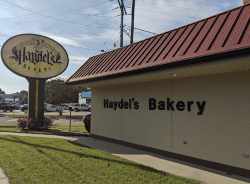 Sign for Haydel's Bakery with a red roof and green grass in front, under a clear blue sky.