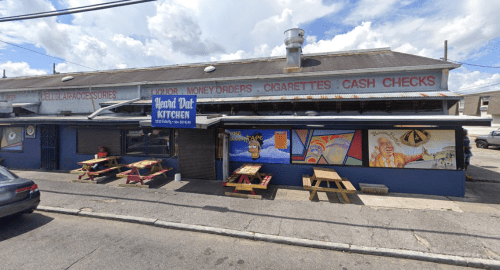 A colorful restaurant exterior with picnic tables, murals, and a sign reading "Head Dat Kitchen."
