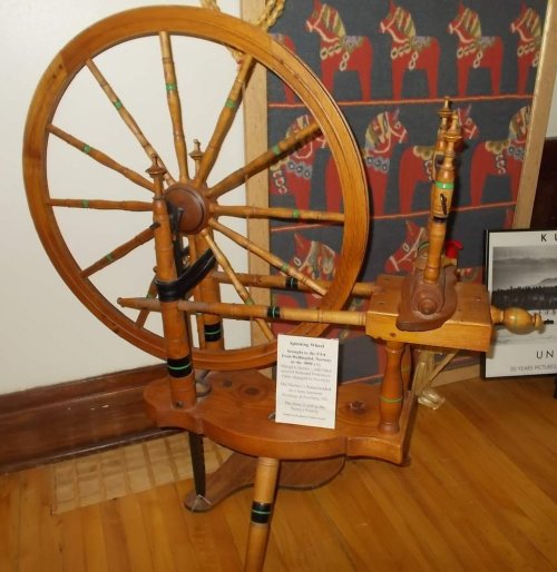 A vintage wooden spinning wheel displayed indoors, with a sign detailing its history and craftsmanship.