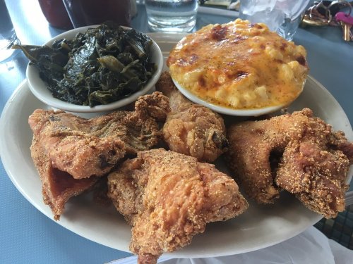 A plate of fried chicken, collard greens, and macaroni and cheese served in bowls.
