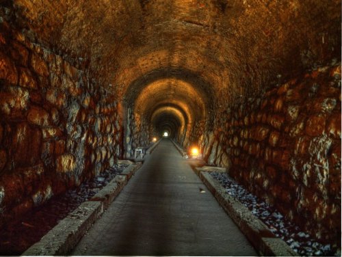 A dimly lit stone tunnel with a smooth path, illuminated by soft lights at the far end.