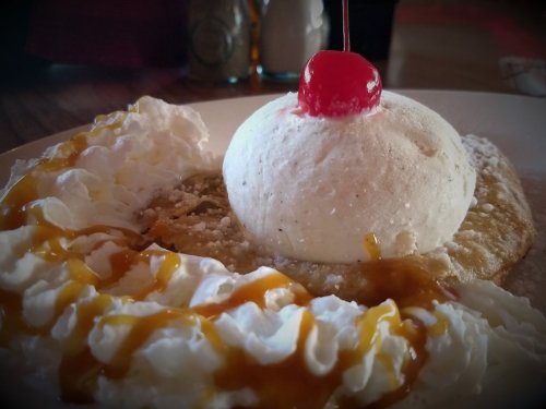 A dessert featuring a scoop of vanilla ice cream topped with a cherry, surrounded by whipped cream and caramel sauce.