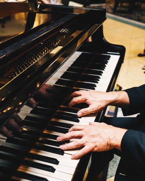 A close-up of hands playing a grand piano, focusing on the black and white keys.