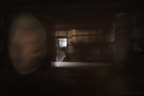 A blurred figure in the foreground with a faint silhouette of a person in a dimly lit, abandoned space.