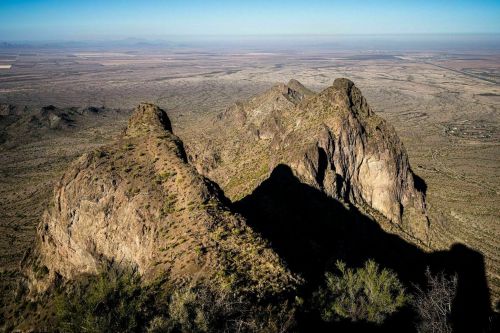 Aerial view of rugged mountain peaks casting shadows over a vast, arid landscape with distant hills.