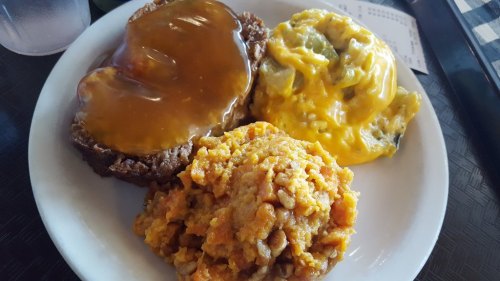 A plate with meatloaf topped with gravy, cheesy vegetables, and a serving of sweet potato mash.